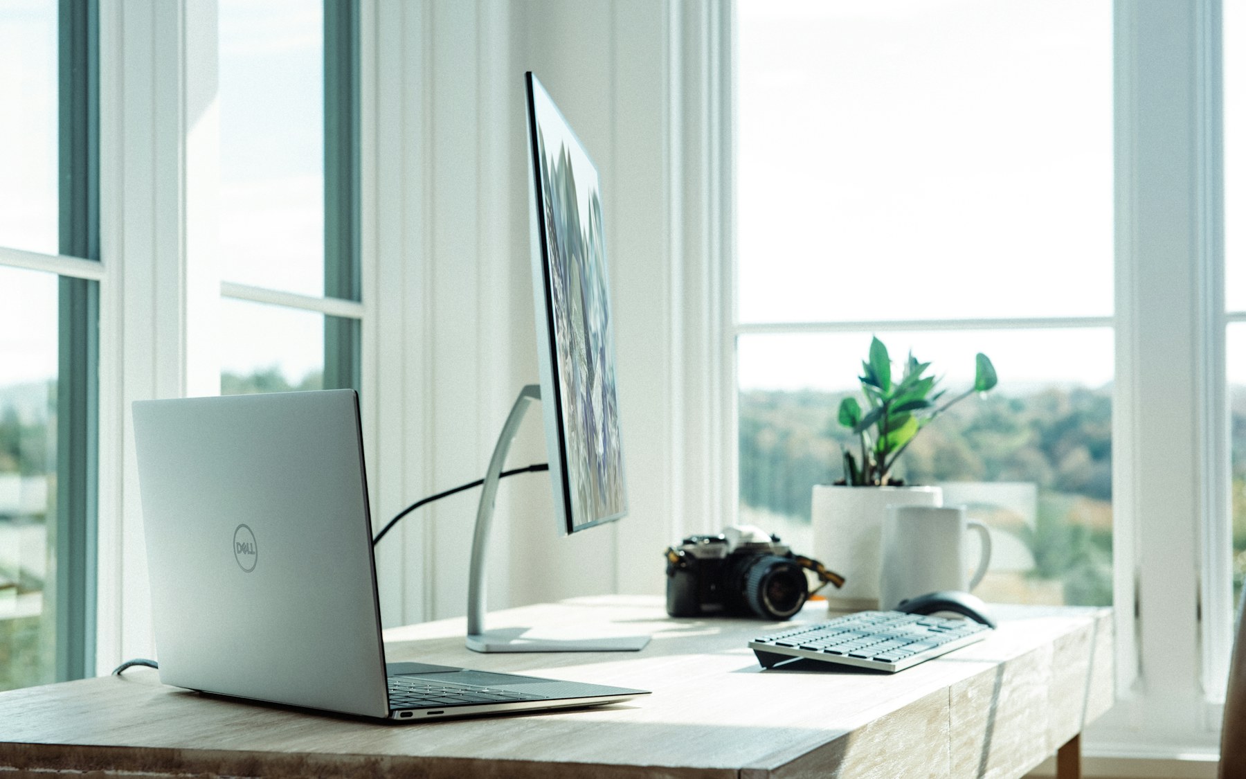 Bright home office desk with a laptop and monitor by a window