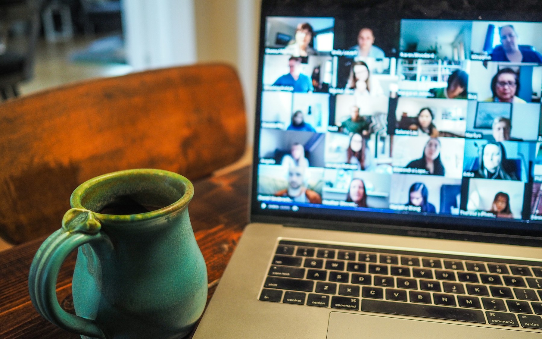 Laptop showing a video meeting with many team members beside a coffee mug